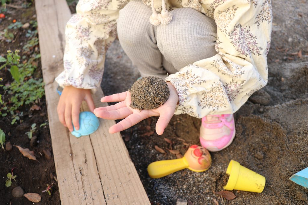 子供が砂場でバイキンマンの型抜きをして見せている写真